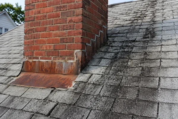 rusted chimney flashing and black algae streaks on an older roof