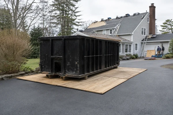 roofing dumpster on boards protecting a driveway during a roof replacement