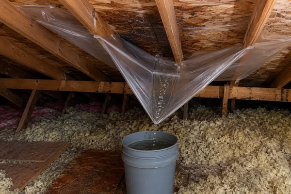 Plastic sheeting steering an attic roof leak into a bucket