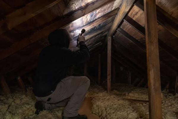 inspecting attic roof deck for a leak with a flashlight