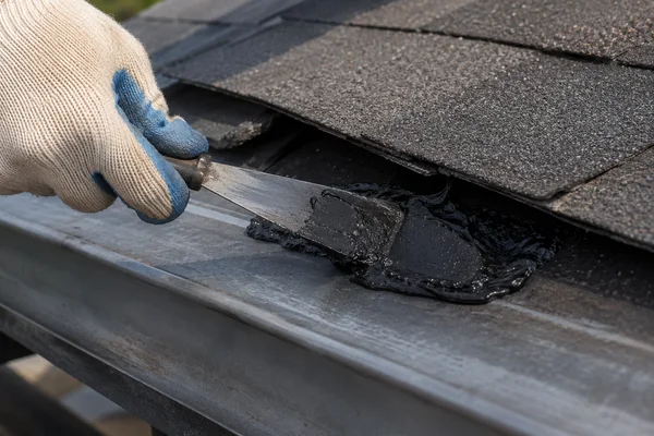 Applying asphalt roofing cement to a lifted shingle